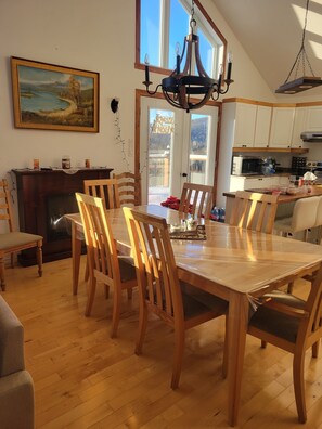 A dining area with a wooden table and chairs, a chandelier, a painting, and a view of the outdoors through a door.