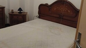 Un dormitori amb un llit de fusta, una tauleta de nit amb una làmpada i un prestatge.