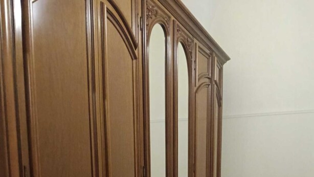 Una habitació amb un armari de fusta gran, una cadira i un terra de rajoles.