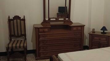 A bedroom with a wooden bed, a wooden dresser with a mirror, a striped chair, and a small table with a lamp.