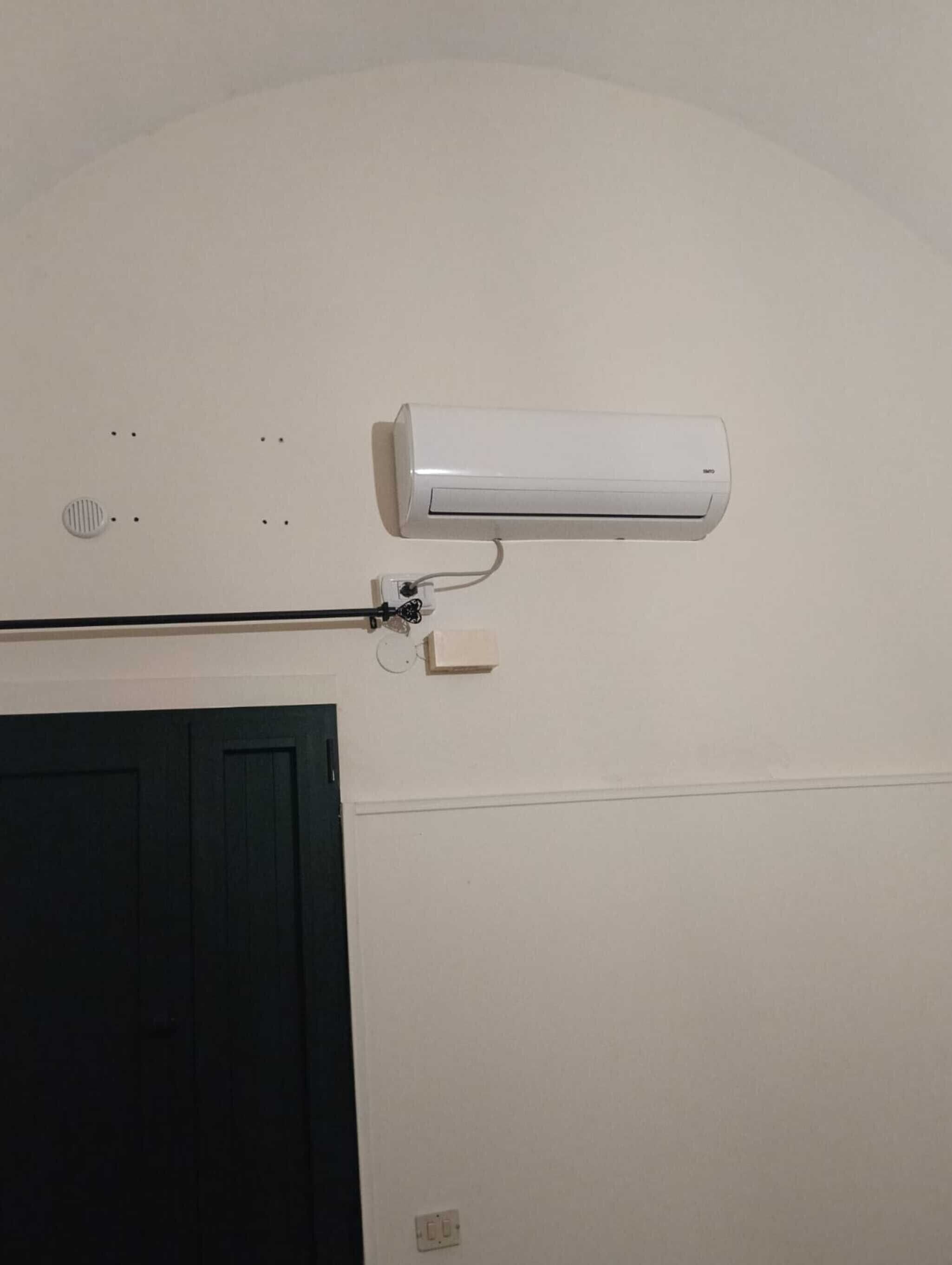 Eine Wand-Klimaanlage mit Stromkabel, Lüftungsgitter und einer Tür darunter.