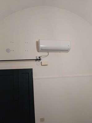 Eine Wand-Klimaanlage mit Stromkabel, Lüftungsgitter und einer Tür darunter.