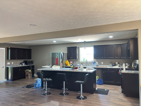 A modern kitchen with dark cabinets, a central island with stools, a sink, and a window providing natural light.