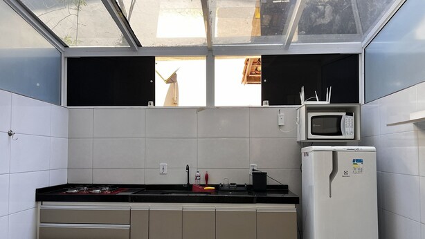 Una cocina compacta con armarios blancos, una encimera negra, un microondas y un refrigerador.