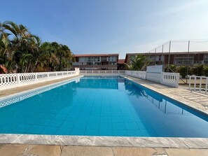 A rectangular swimming pool with a tiled edge, surrounded by a white fence and palm trees.
