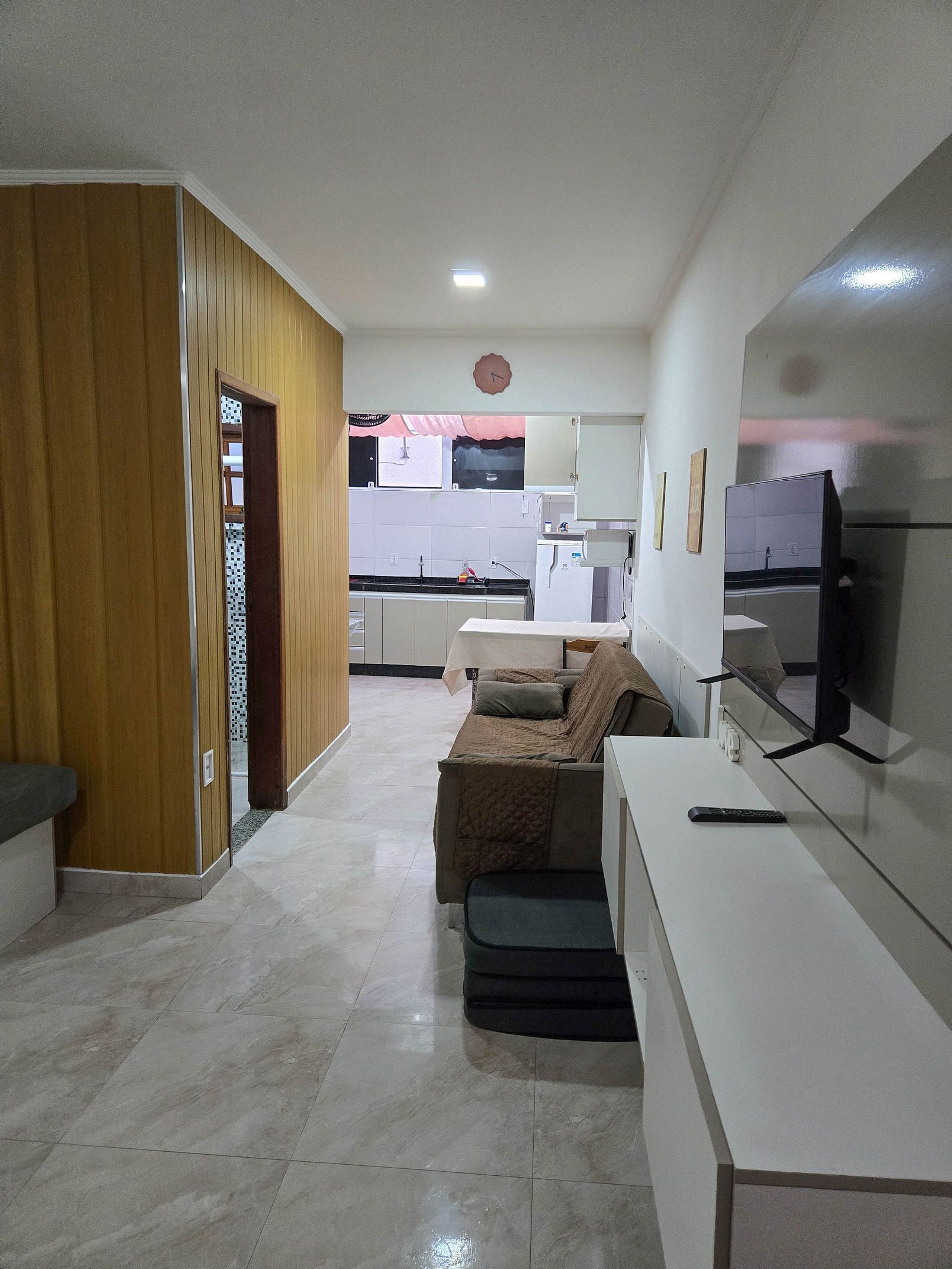 Una sala de estar moderna con un sofá, un televisor y una cocina al fondo.