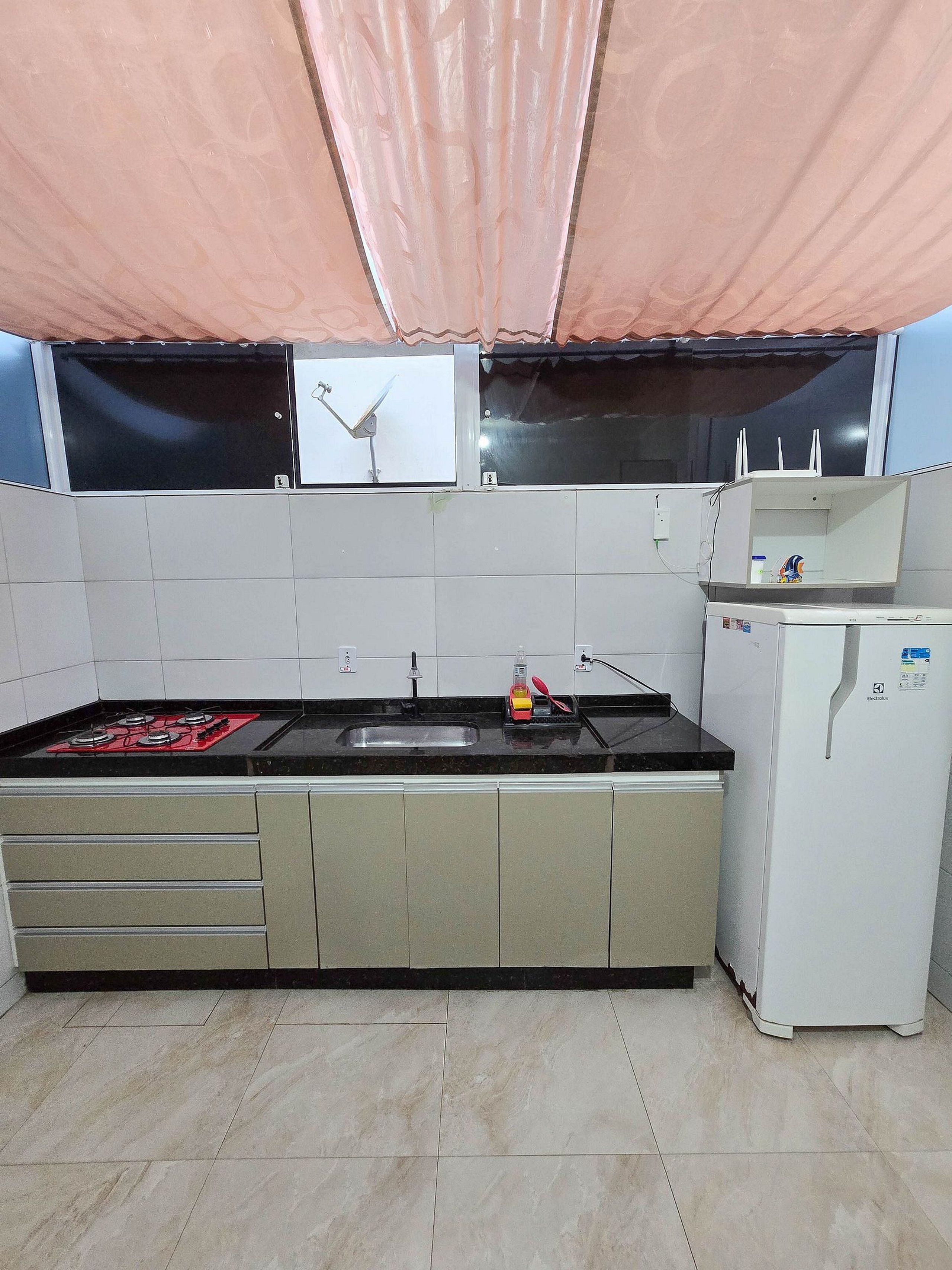 Una cocina con estufa a gas, un lavamanos, refrigerador y una ventana con cortina.
