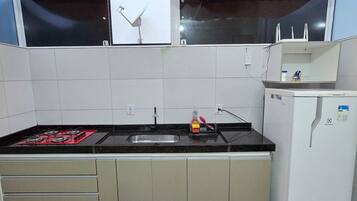 Una cocina con estufa a gas, un lavamanos, refrigerador y una ventana con cortina.