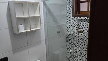 Un baño con inodoro, ducha con mampara de vidrio y pared de azulejos blancos.