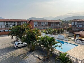 A hotel with a swimming pool, palm trees, and a view of mountains. - Conforto piscina e perto da praia (Ubatuba)