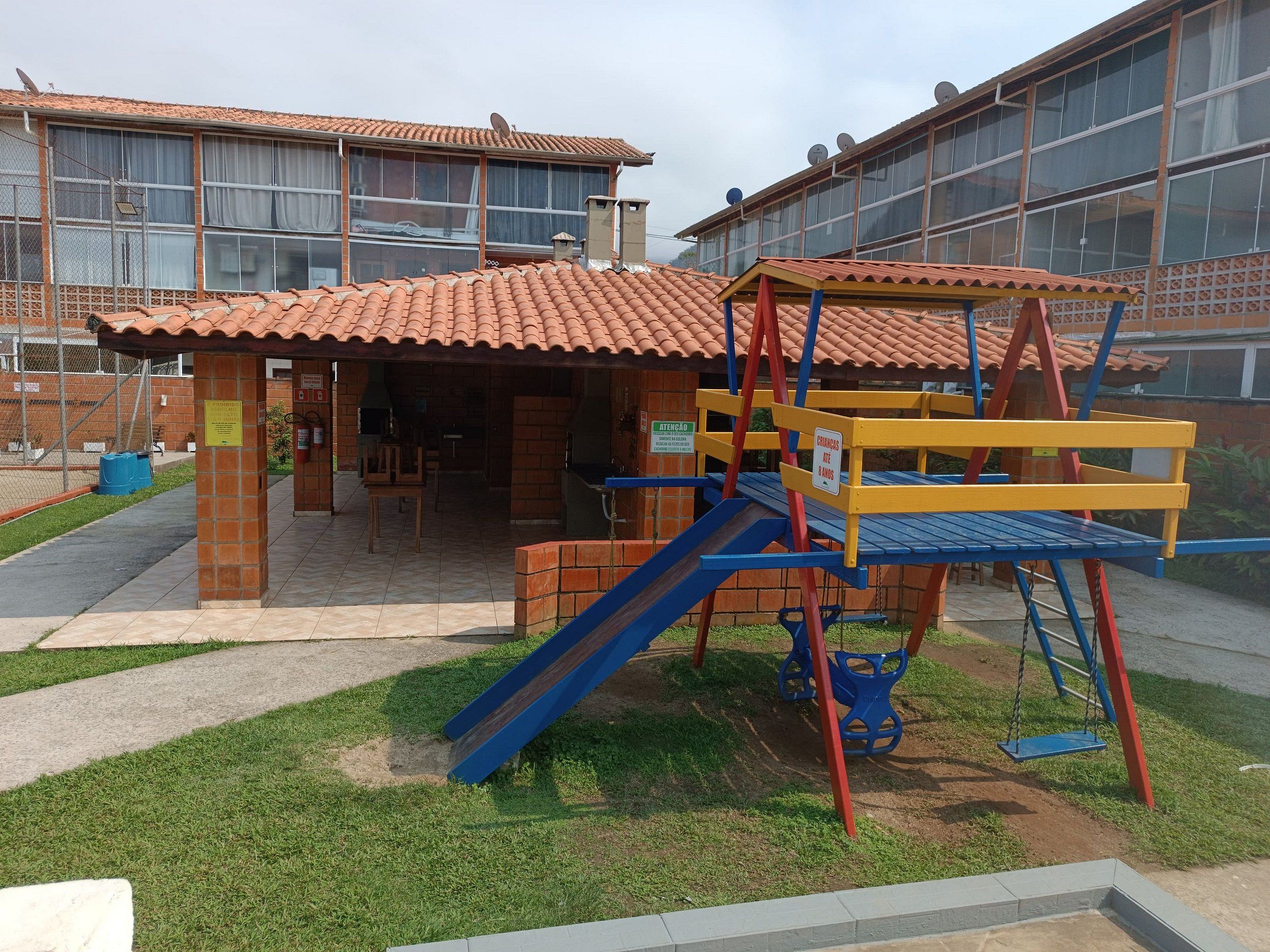 Un terrain de jeux équipé d’un toboggan et d’une structure d’escalade, entouré d’un bâtiment doté de grandes fenêtres et d’un toit en tuiles.