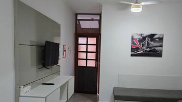 Una sala de estar moderna con una televisión de pantalla plana, un banco, un sofá y una puerta que da a otra habitación.