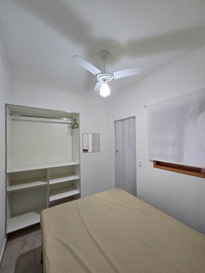 A room with a bed, a ceiling fan, a wardrobe, and a window with a blind. - Conforto piscina e perto da praia (Ubatuba)