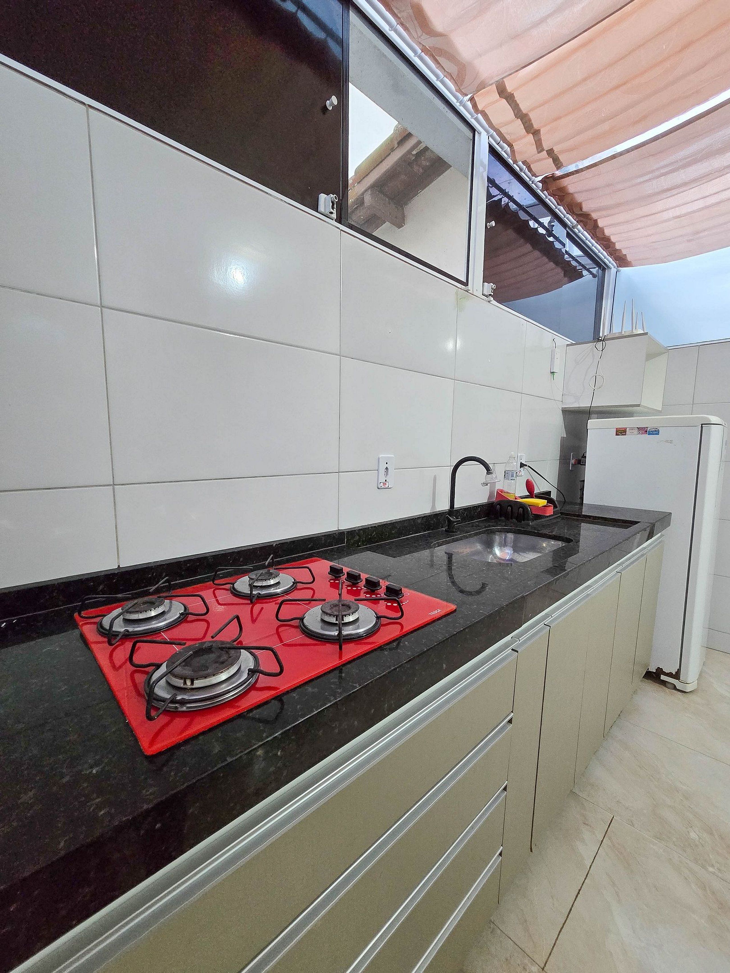 A kitchen with a black countertop, a red gas stove, and white cabinets.