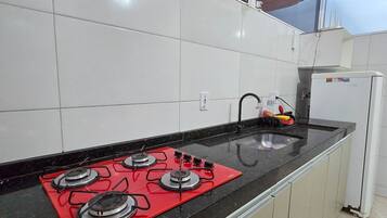 A kitchen with a black countertop, a red gas stove, and white cabinets.