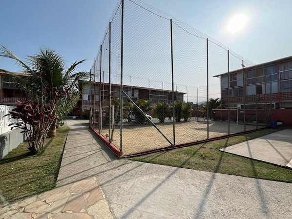 A fenced outdoor area with a concrete floor, surrounded by buildings with multiple windows and a clear sky.