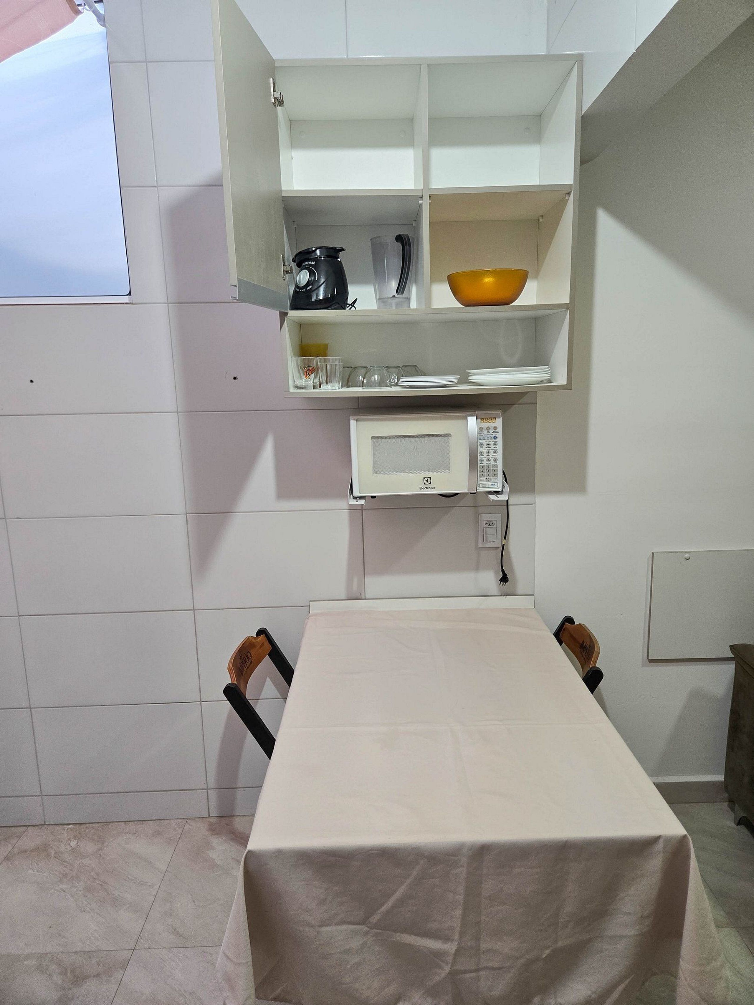 Un angolo cottura accessoriato con forno a microonde, macchina del caffè e una ciotola sullo scaffale.