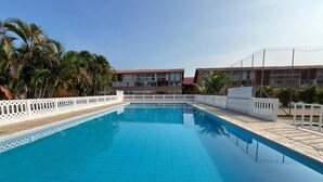 Una piscina rectangular con borde de azulejos, rodeada por una valla blanca y palmeras.
