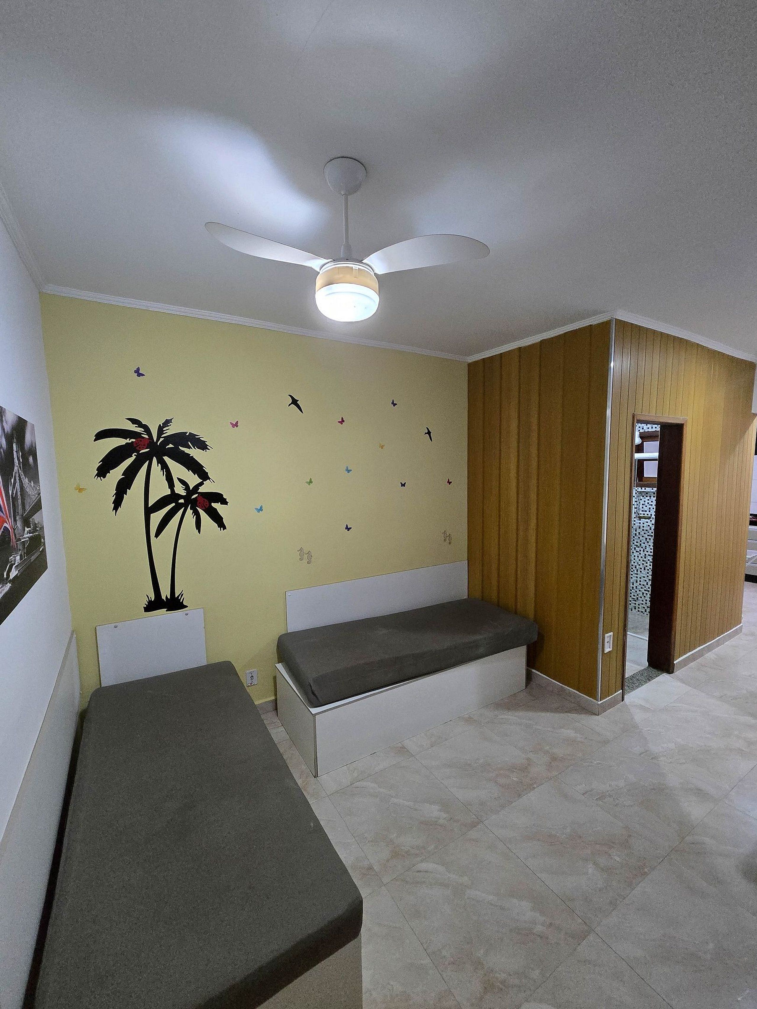 Una habitación con cama, un banco, un ventilador de techo y una pared decorada con adhesivos de mariposas.