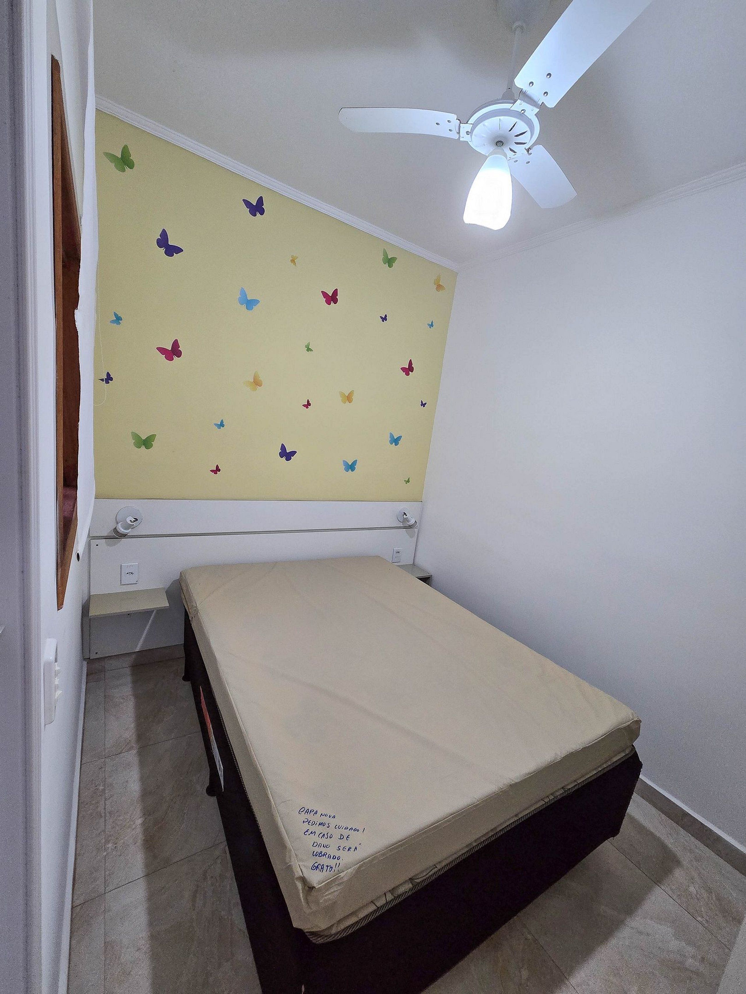 A room with a bed, a ceiling fan, and butterfly wall decals.