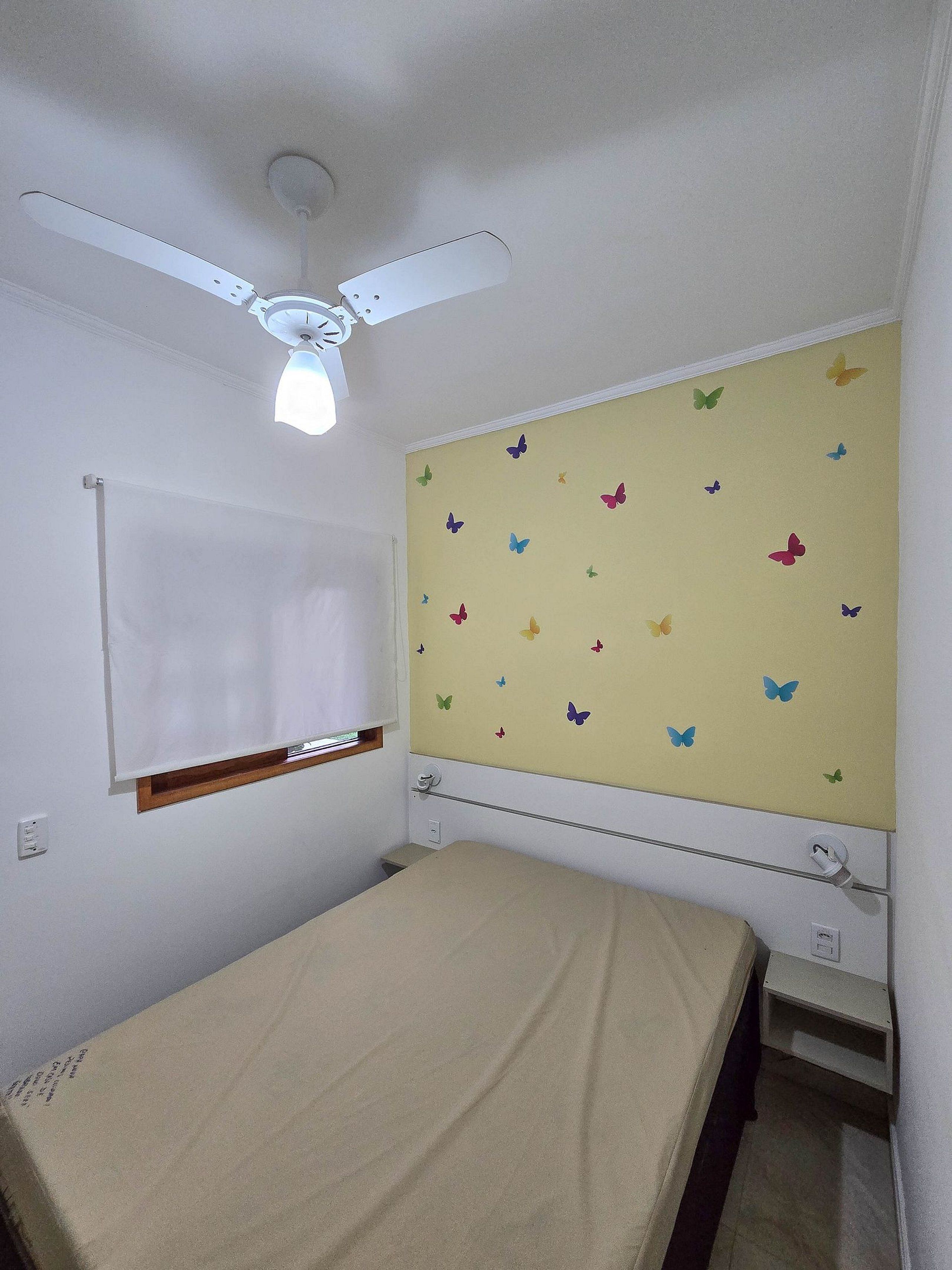 Ein Schlafzimmer mit einem Bett, einem Deckenventilator, einem Fenster mit Jalousien und einer Wand mit Schmetterlingsaufklebern.