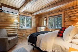 Ein Schlafzimmer in einer Blockhütte mit einem Bett, einem Sessel, einem Nachttisch und einem Fenster.