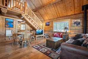 Ein rustikales Blockhaus-Interieur mit einer Holztreppe, einem Essbereich, einer Couch und einem Kamin.