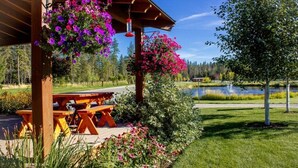 Ein hölzernes Pavillon mit hängenden Blumenkörben, einem Picknicktisch und Blick auf einen See.