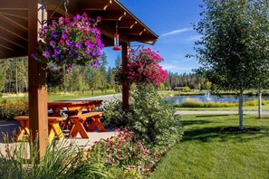 Ein hölzernes Pavillon mit hängenden Blumenkörben, einem Picknicktisch und Blick auf einen See.