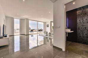 Ein geräumiger Wohnbereich mit einem großen Glasfenster zum Balkon, eine moderne Küche mit schwarzer Strukturwand und ein sauberes, minimalistisches Design.