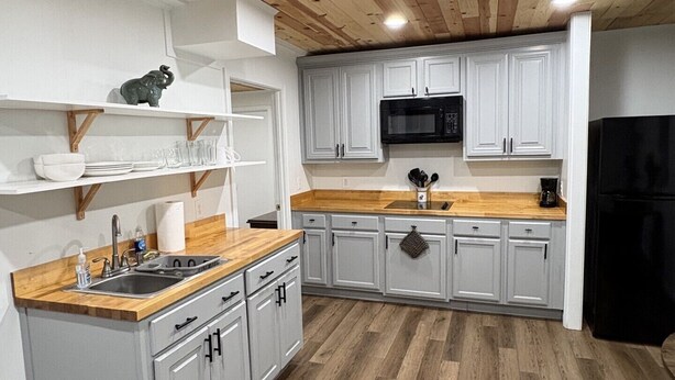 A kitchen with wooden ceiling beams, white cabinets, a black refrigerator, and a wooden countertop. - Guest Suite in Northport Downtown (Northport)