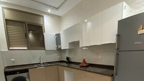 A modern kitchen with a washing machine, a refrigerator, and a window with blinds. - A comfortable apartment near the sea (Essaouira)