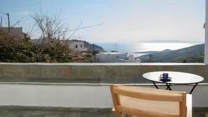 Un balcon avec une table et une chaise, donnant sur un paysage côtier avec des bâtiments et une étendue d’eau.