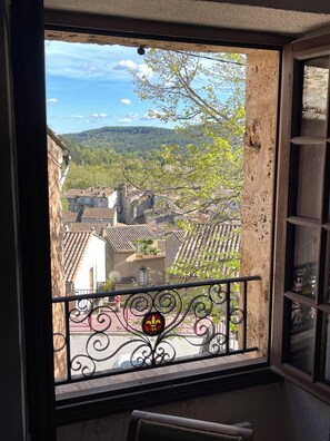 Ein Balkon mit schmiedeeisernen Geländern, Blick auf eine Stadt mit Terrakotta-Dächern und ein Baum mit grünen Blättern.
