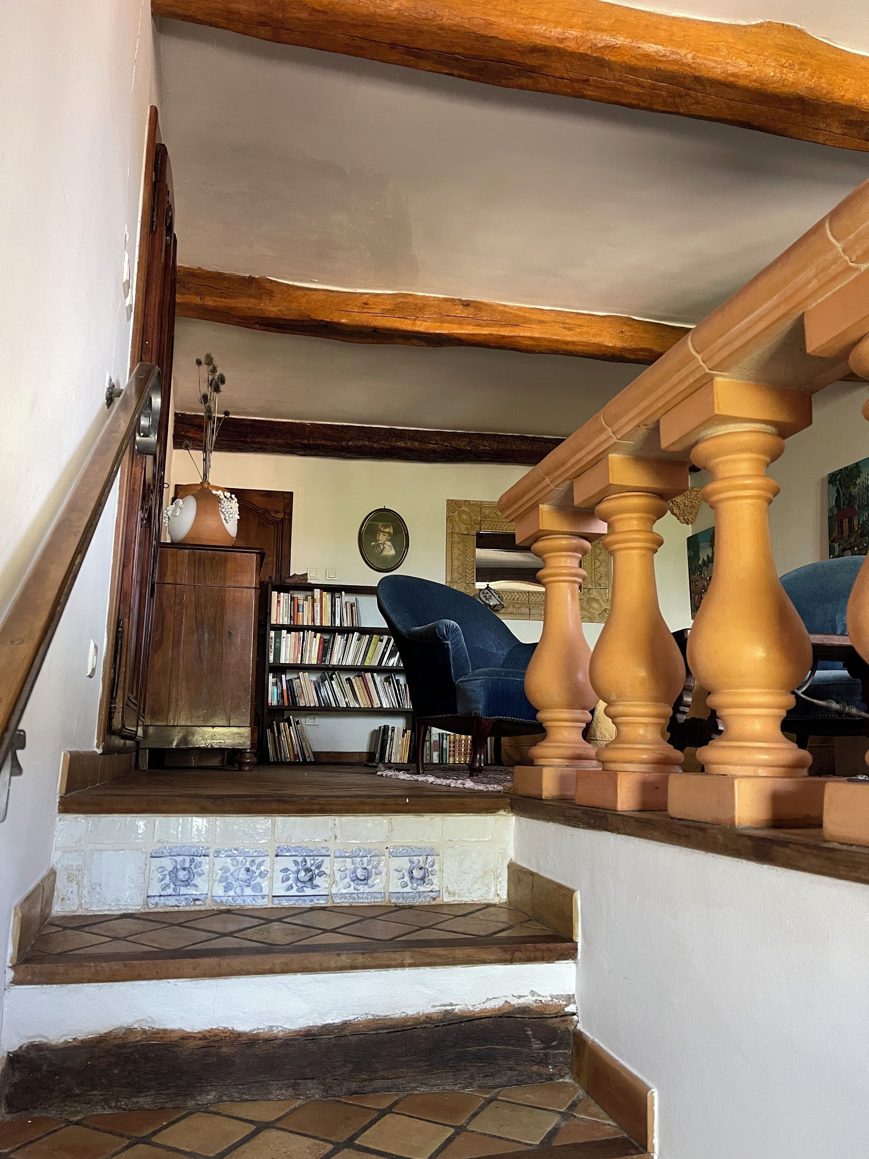 Eine Treppe mit Holzspindeln, ein blauer Sessel, ein Bücherregal und ein Fliesenboden.