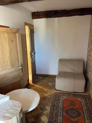 Ein Zimmer mit Holztür, einem beigefarbenen Sofa, einem gemusterten Teppich und Fliesenboden.