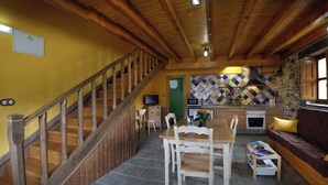 Una escalera de madera que lleva a un comedor con una mesa y sillas, una cocina con pared de piedra, y un sofá con cojines.