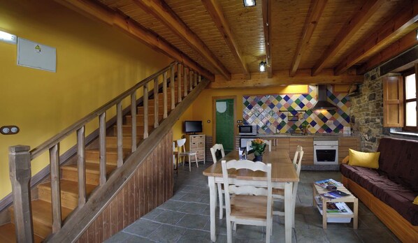A wooden staircase leading to a dining area with a table and chairs, a kitchen with a stone wall, and a sofa with cushions. - EL MIRADOR DE LLANANZANES (Aller)