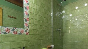 Un baño con pared de azulejos verdes, un lavamanos blanco, un inodoro y una zona de ducha.
