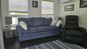 A room with a blue sofa, a black chair, a small table, and a window with blinds.
