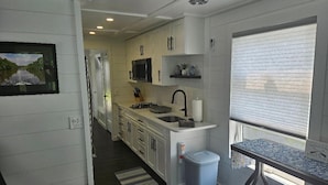 A modern kitchen with white cabinetry, a microwave, a sink, and a window with blinds.
