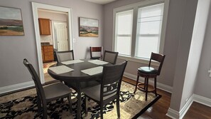 Un coin repas avec une table ronde, six chaises et deux tableaux accrochés au mur.