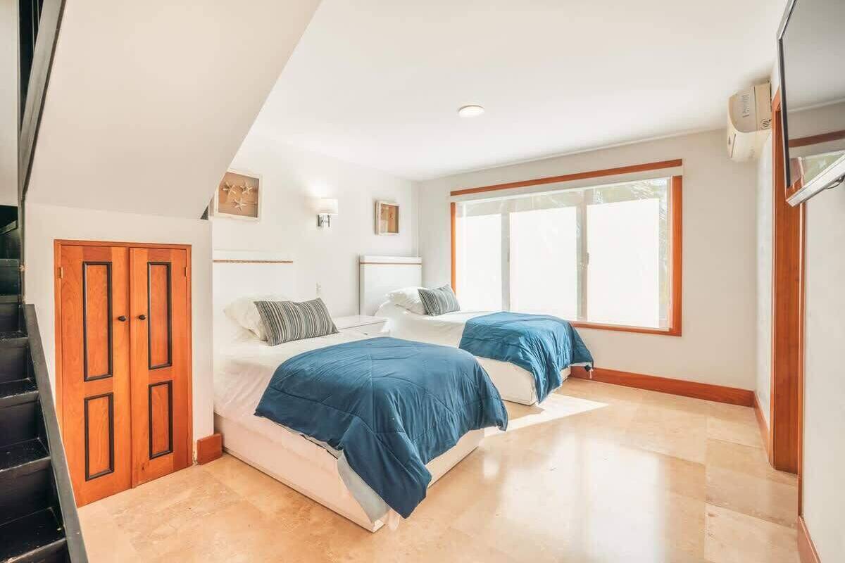 A bedroom with two beds, a wooden door, and a large window.