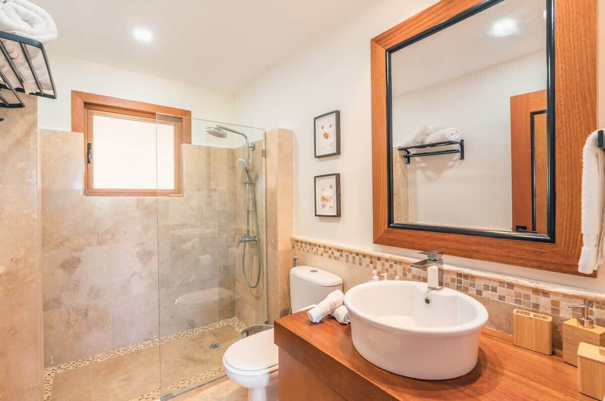 A modern bathroom with a glass-enclosed shower, a large mirror, and a wooden vanity.