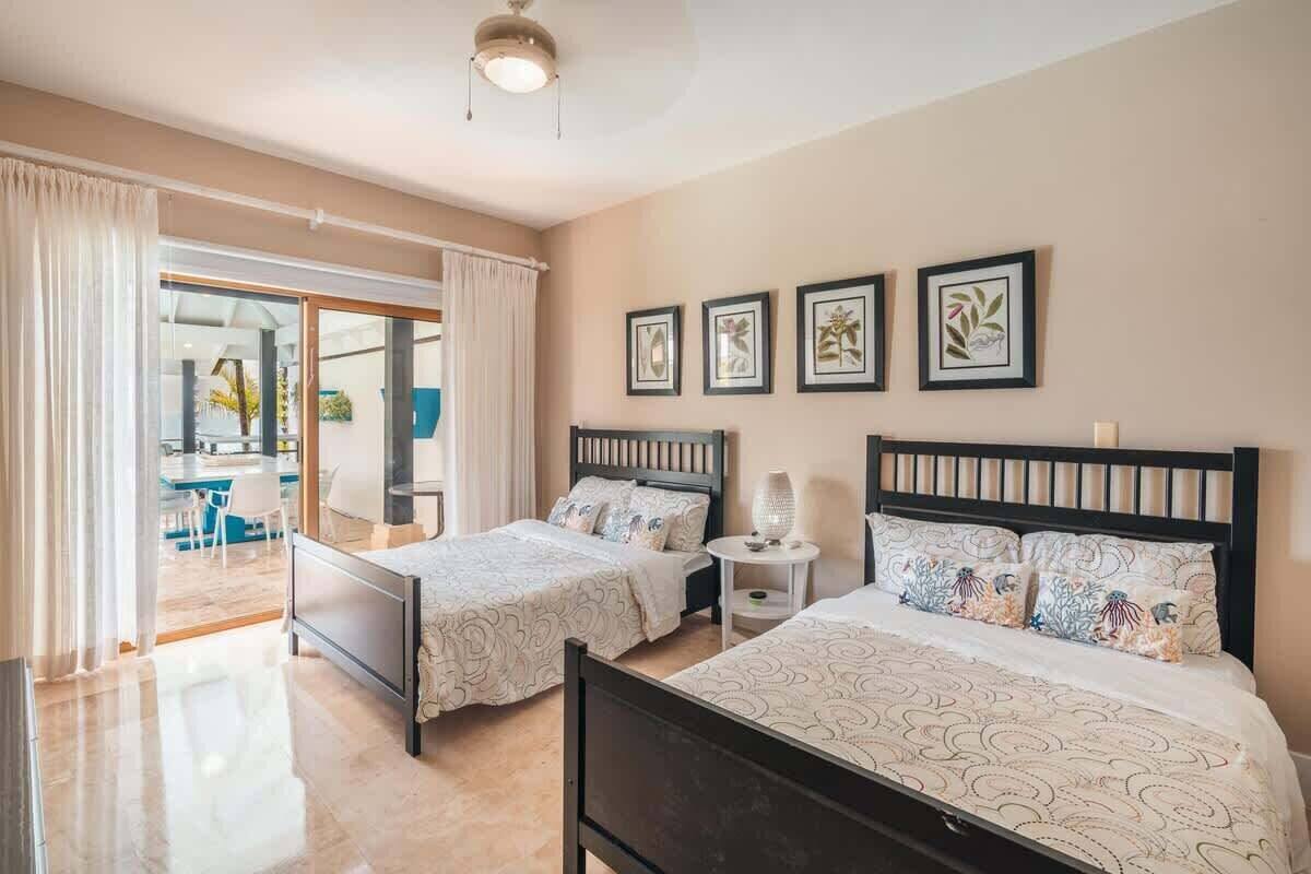 A hotel room with two beds, a small bedside table with a lamp, and a large sliding glass door leading to a balcony.