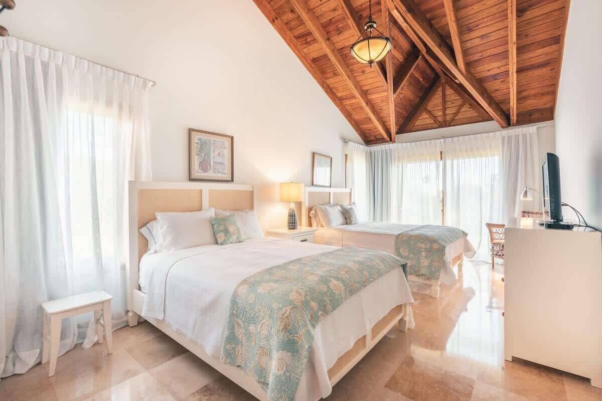 A bedroom with two beds, a wooden ceiling, and a bedside table with a lamp.