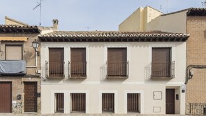 A building with a tiled roof, multiple windows with metal bars, and a door. - Apartamentos Granadal. Bajo (Toledo)