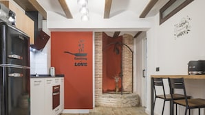 A modern kitchen with a red accent wall, a black refrigerator, and a dining area with two chairs. - Apartamentos Granadal. Bajo (Toledo)