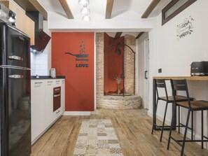 Eine moderne Küche mit roter Akzentwand, einem schwarzen Kühlschrank und einer Essecke mit zwei Stühlen.