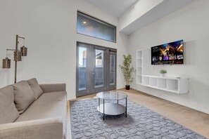 Ein modernes Wohnzimmer mit einer Couch, einem Glastisch, einem an der Wand montierten Fernseher und einer Topfpflanze.